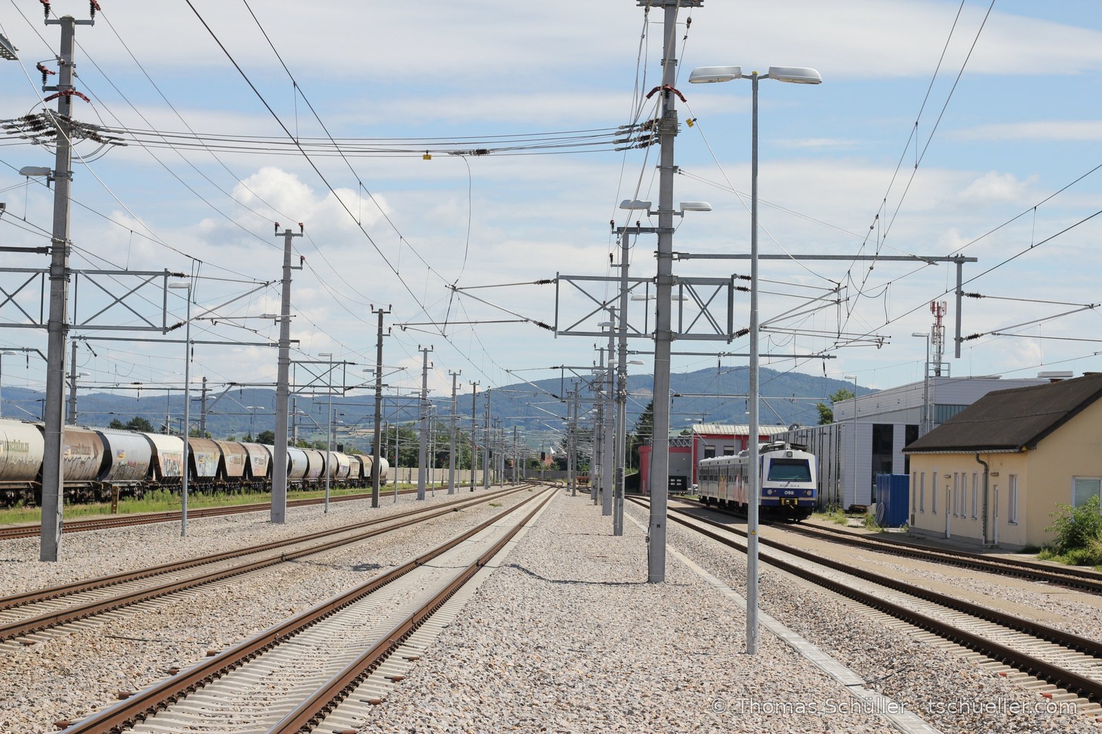 Gleisfeld mit Oberleitungsmasten, Triebwagen und Hügeln im Hintergrund